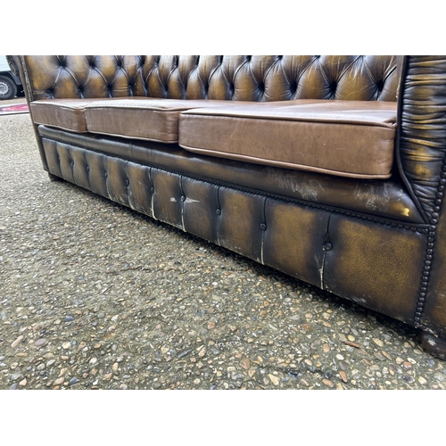 63 - A golden brown leather chesterfield three seater sofa