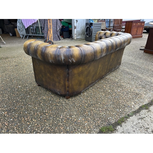 63 - A golden brown leather chesterfield three seater sofa