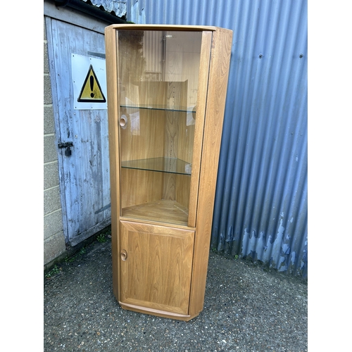 32 - An ercol light elm corner cabinet with glazed door and illuminating interior