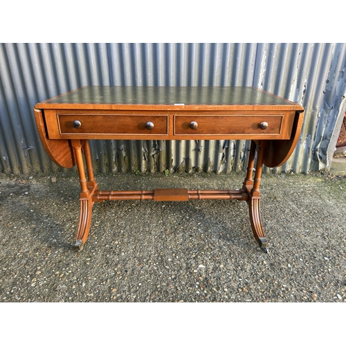 52 - A reproduction yew wood writing table with drop leaf ends and a green leather top