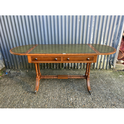 52 - A reproduction yew wood writing table with drop leaf ends and a green leather top