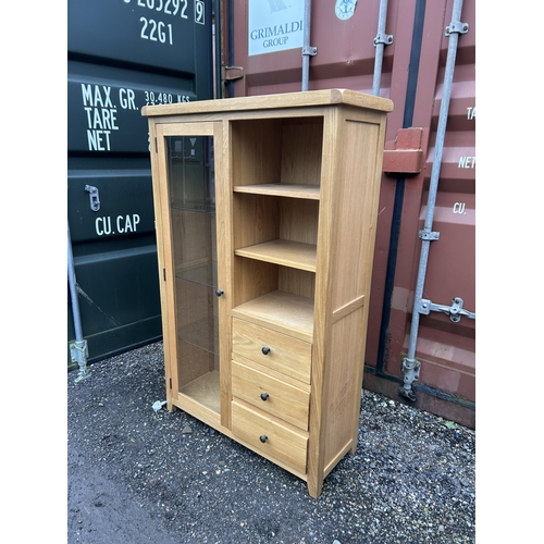 26 - A glazed light oak bookcase cabinet with three drawers 106x40x156