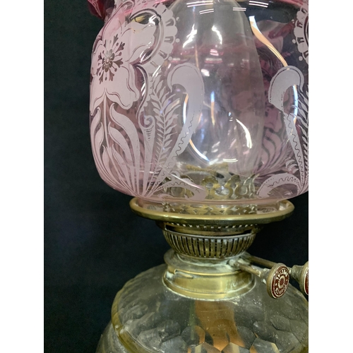 634 - Brass oil lamp with cranberry shade, height 55cms (crack to bottom of shade)