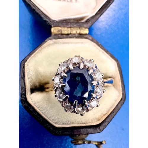 115 - A Sapphire and diamond cluster dress ring on 18ct white and yellow gold.The oval cut sapphire aprox ... 