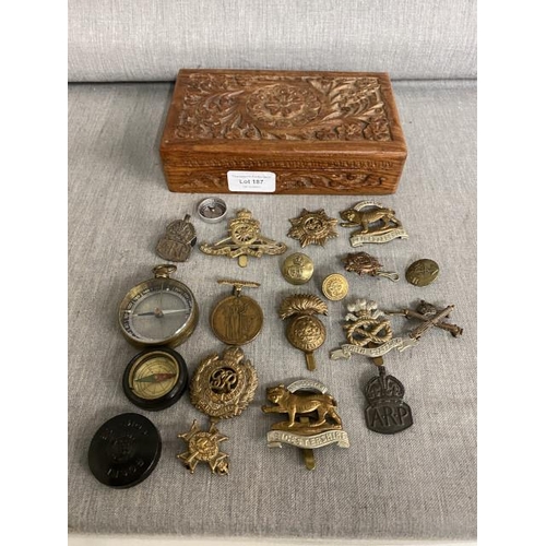 187 - Carved box of Militaria collectables inc. WWII cap badges, 3 compasses, air raid precaution wardens ... 