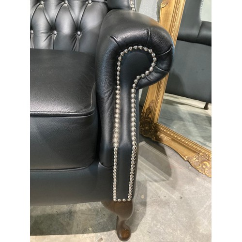 145 - Hand made black leather button back Chesterfield wing armchair 108H 80W 73D and a matching footstool... 