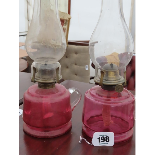 198 - Pair of Cranberry Glass Paraffin Lamps with Integral Carrying Hoop Tallest Approximately 12 Inches