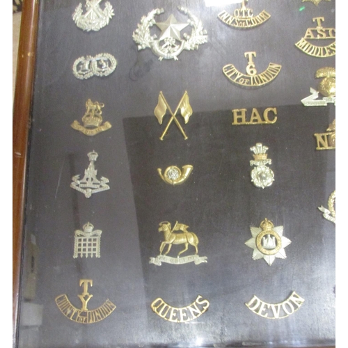 70 - Collection in large wood and glass frame of metal cap badges, shoulder titles etc, including QV 1st ... 