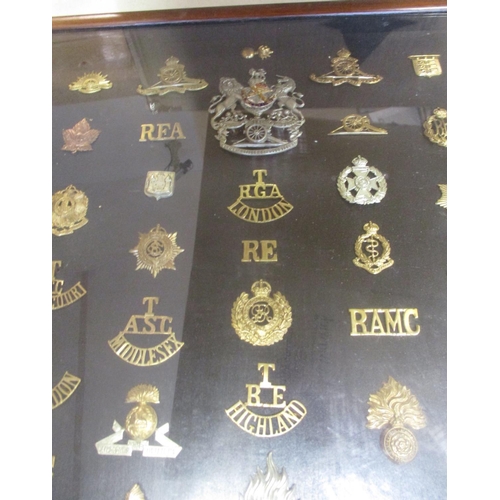 70 - Collection in large wood and glass frame of metal cap badges, shoulder titles etc, including QV 1st ... 