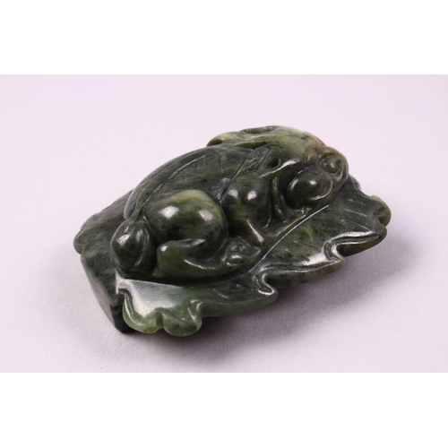 119 - A CHINESE CARVED JADE BELT BUCKLE / DECORATION OF A RECUMBENT KYLIN, upon a leaf, 6.5cm.