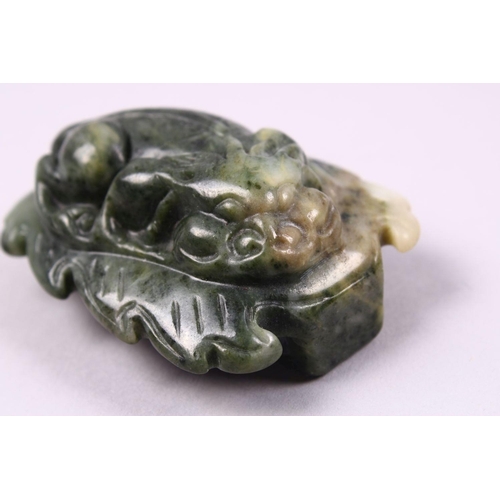 119 - A CHINESE CARVED JADE BELT BUCKLE / DECORATION OF A RECUMBENT KYLIN, upon a leaf, 6.5cm.