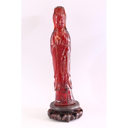 217 - TWO CHINESE CHERRY AMBER FIGURES OF GUANYIN, on carved wooden bases, 32cm and 33cm high.