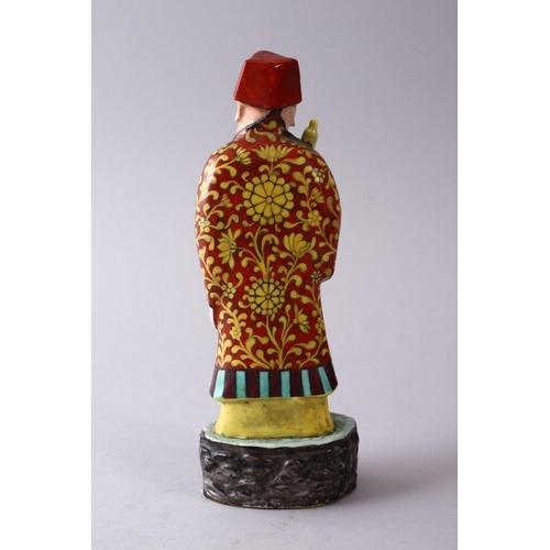 335 - A CHINESE FAMILLE ROSE POTTERY FIGURE OF A SCHOLAR, holding a scroll upon a stylized base, 22cm high... 