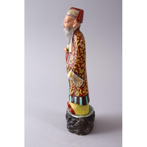 335 - A CHINESE FAMILLE ROSE POTTERY FIGURE OF A SCHOLAR, holding a scroll upon a stylized base, 22cm high... 