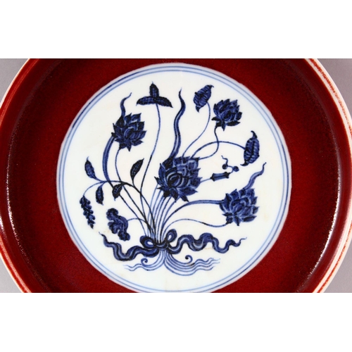 436 - A MING STYLE COPPER RED CIRCULAR PORCELAIN DISH, the central blue and white panel painted with lotus... 