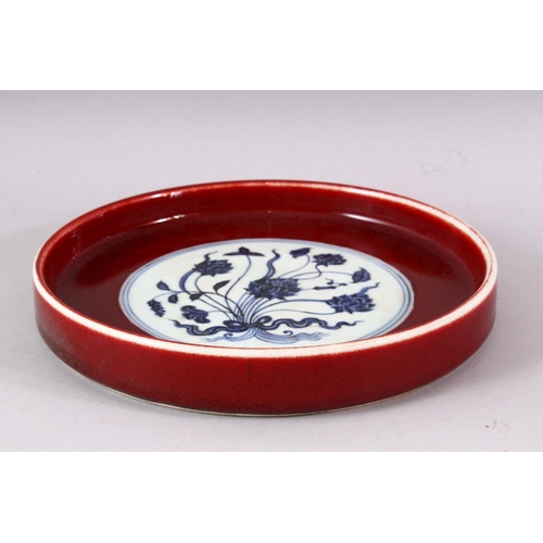 436 - A MING STYLE COPPER RED CIRCULAR PORCELAIN DISH, the central blue and white panel painted with lotus... 