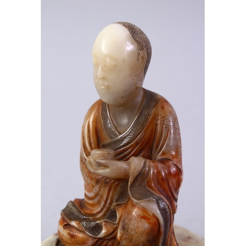 472A - A GOOD CHINESE CARVED SOAPSTONE FIGURE OF ROHAN, in a seated position holding a vessel, with a carve... 