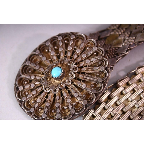 643 - AN EASTERN WHITE METAL BELT, the oval filigree buckle mounted with a turquoise cabouchon stone, 80cm... 