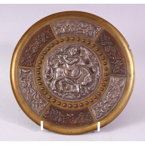 613 - AN INDIAN BRASS CIRCULAR DISH, overlaid with white metal and copper panels, the centre depicting a f... 