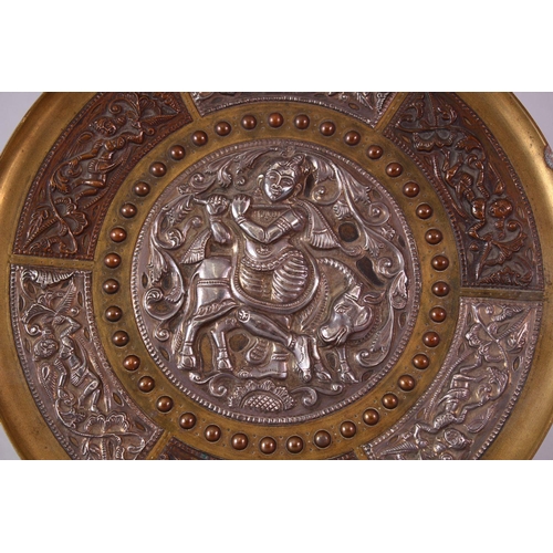 613 - AN INDIAN BRASS CIRCULAR DISH, overlaid with white metal and copper panels, the centre depicting a f... 