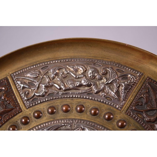 613 - AN INDIAN BRASS CIRCULAR DISH, overlaid with white metal and copper panels, the centre depicting a f... 