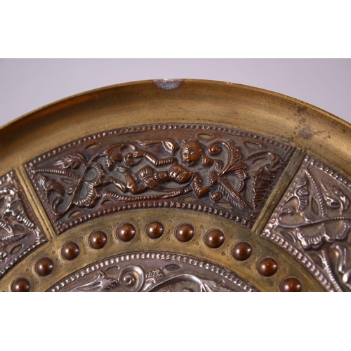 613 - AN INDIAN BRASS CIRCULAR DISH, overlaid with white metal and copper panels, the centre depicting a f... 