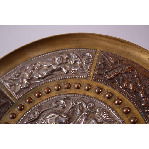 613 - AN INDIAN BRASS CIRCULAR DISH, overlaid with white metal and copper panels, the centre depicting a f... 