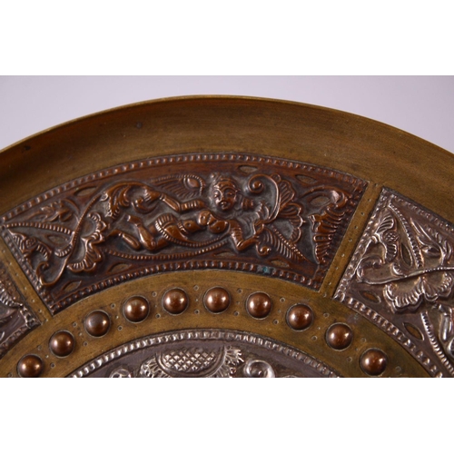 613 - AN INDIAN BRASS CIRCULAR DISH, overlaid with white metal and copper panels, the centre depicting a f... 