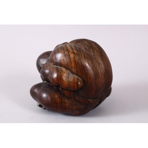 63 - AN ORIENTAL CARVED HARDWOOD FIGURE OF A FIGURE, in a seated downward position with its hands coverin... 