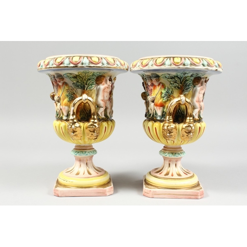 98 - A PAIR OF CAPODIMONTE STYLE POTTERY URNS AND COVERS  with panels of cupids. 9 ins. high.