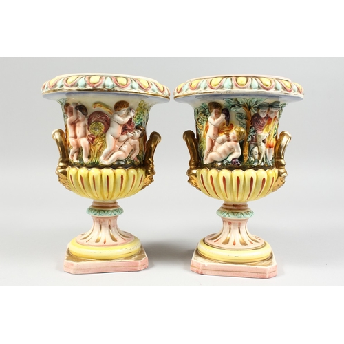 98 - A PAIR OF CAPODIMONTE STYLE POTTERY URNS AND COVERS  with panels of cupids. 9 ins. high.