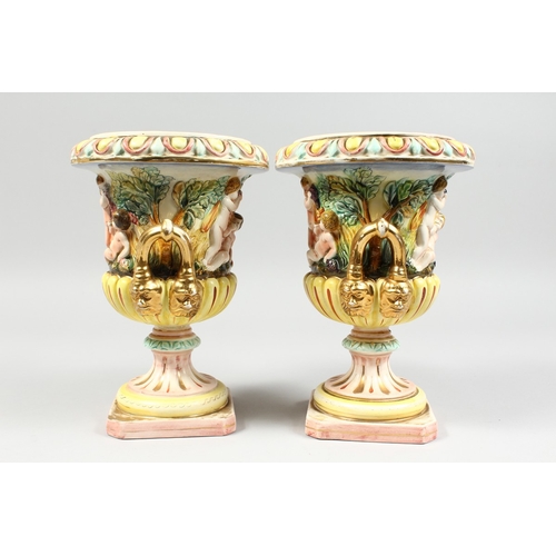 98 - A PAIR OF CAPODIMONTE STYLE POTTERY URNS AND COVERS  with panels of cupids. 9 ins. high.