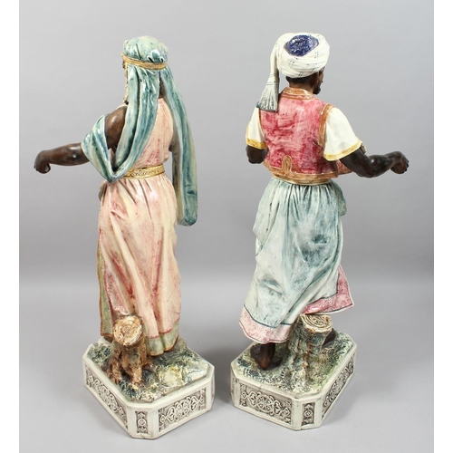 1215 - A VERY GOOD PAIR OF LARGE MAJOLICA POTTERY FIGURES OF AN ARAB MAN AND YOUNG GIRL standing holding to... 