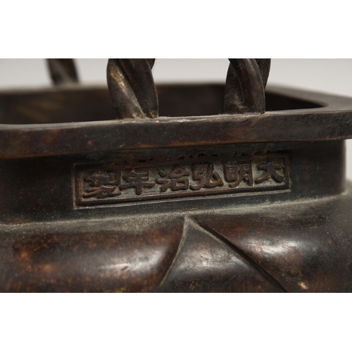 1274 - A CHINESE BRONZE SQUARE CENSER with rope handles on four curving legs, the sides with calligraphy.