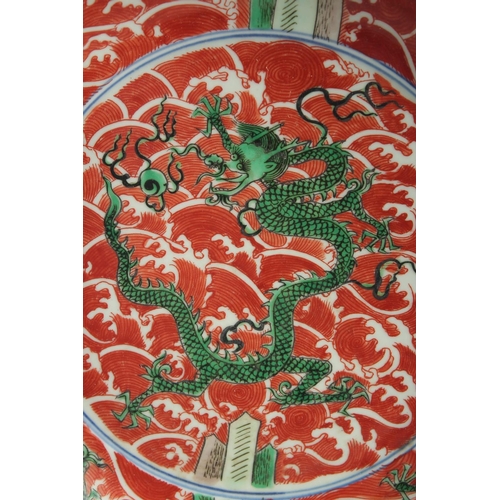 1251 - A CHINESE IRON RED GROUND PORCELAIN DISH painted with green dragons on stylised waves. 24.5cm diamet... 