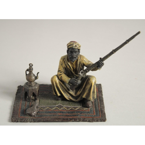 1569 - A COLD CAST MODEL OF A MAN holding a gun and sitting on a carpet. 5ins high.