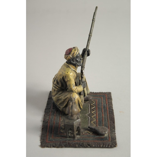 1569 - A COLD CAST MODEL OF A MAN holding a gun and sitting on a carpet. 5ins high.