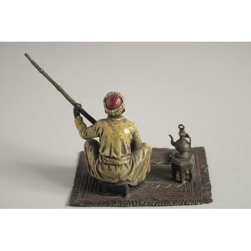 1569 - A COLD CAST MODEL OF A MAN holding a gun and sitting on a carpet. 5ins high.