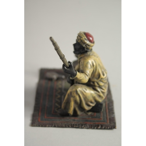 1569 - A COLD CAST MODEL OF A MAN holding a gun and sitting on a carpet. 5ins high.