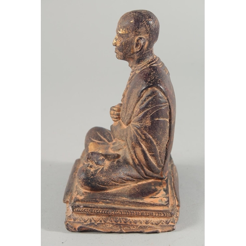 24 - A TIBETAN CARVED STONE SEATED FIGURE, with traces of gold paint, inscribed to the base, 18.5cm high.