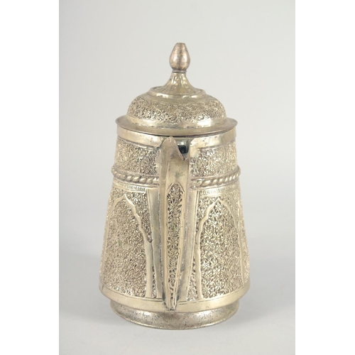 40 - AN ISLAMIC WHITE METAL LIDDED JUG, embossed and chased decoration, 25cm high.