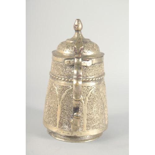 40 - AN ISLAMIC WHITE METAL LIDDED JUG, embossed and chased decoration, 25cm high.