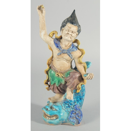 227 - A CHINESE FAHUA FIGURE, standing on a fish, 27cm high.