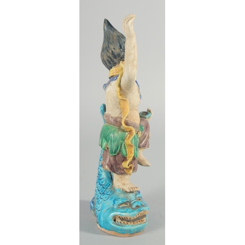 227 - A CHINESE FAHUA FIGURE, standing on a fish, 27cm high.