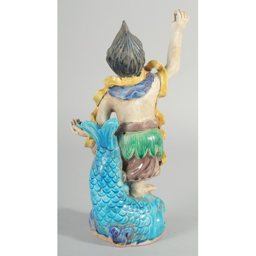 227 - A CHINESE FAHUA FIGURE, standing on a fish, 27cm high.