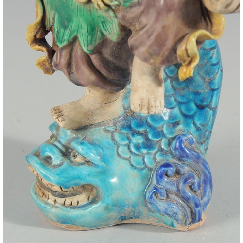 227 - A CHINESE FAHUA FIGURE, standing on a fish, 27cm high.