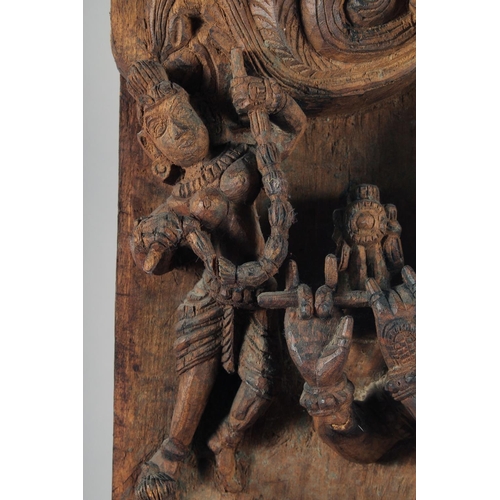 19 - A LARGE INDIAN CARVED WOODEN PANEL, with central deity playing a musical instrument surrounded by fo... 