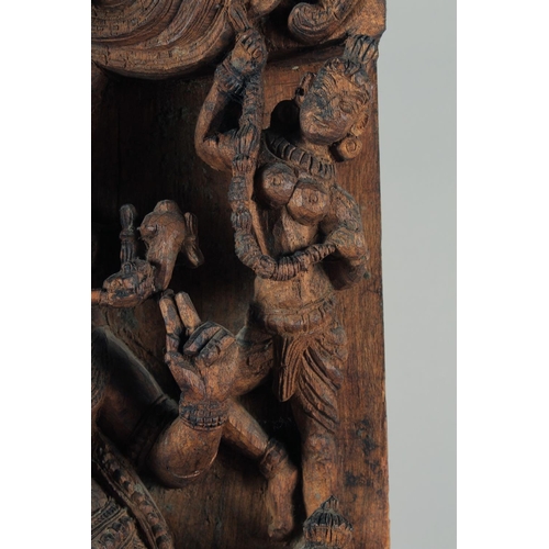 19 - A LARGE INDIAN CARVED WOODEN PANEL, with central deity playing a musical instrument surrounded by fo... 