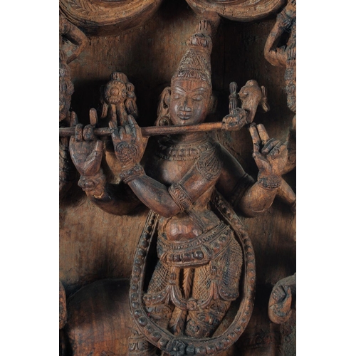 19 - A LARGE INDIAN CARVED WOODEN PANEL, with central deity playing a musical instrument surrounded by fo... 