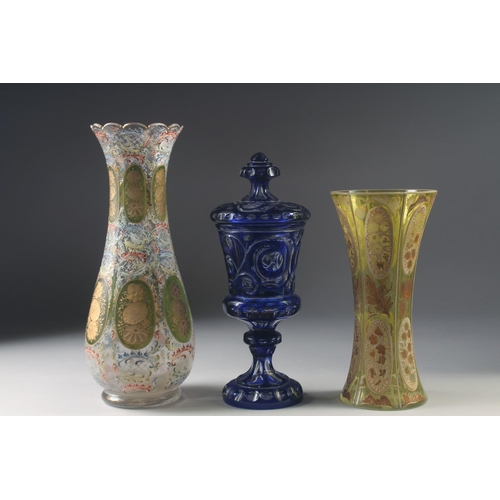 1043 - THREE VARIOUS BOHEMIAN GLASS VASES one with a cover. 13ins, 10ins & 9.5ins high.